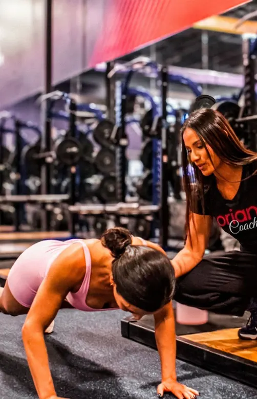 Oriana corrigiendo la técnica de una clienta durante una plancha en el gym